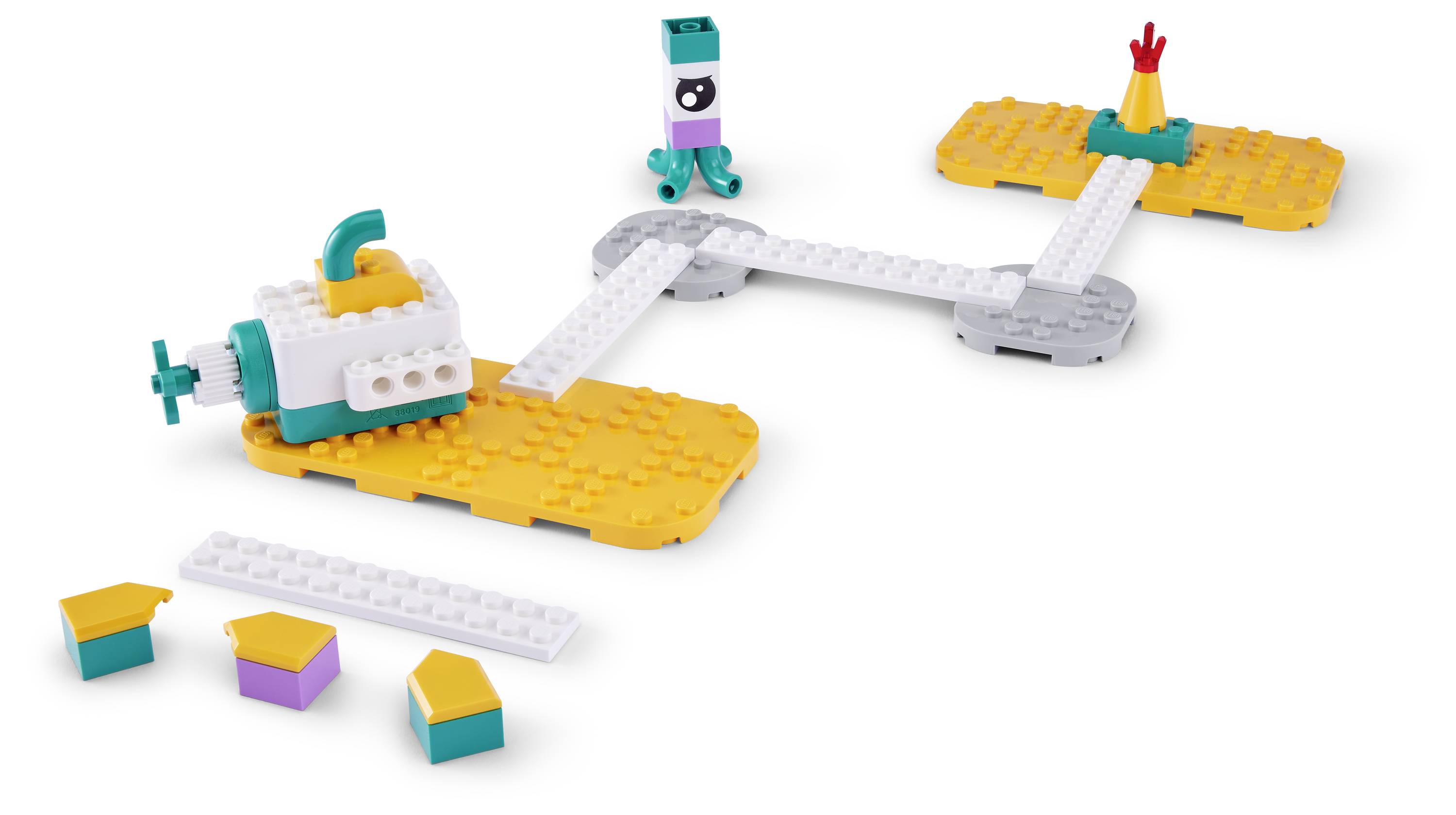 Buntes LEGO-ähnliches Raumschiff-Spielzeug auf weißem Hintergrund mit verbundenen orange- und grauen Plattformen, einer kleinen zentralen roboterartigen Figur und losen Bausteinen darunter.