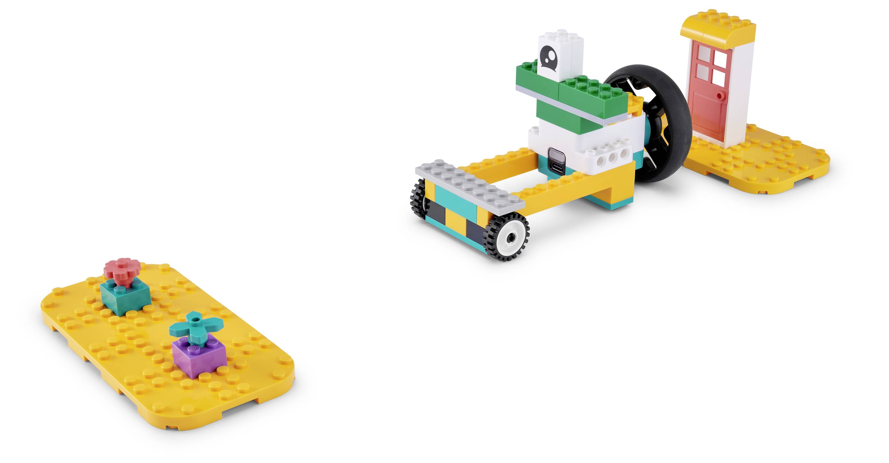 Foto von zwei LEGO-ähnlichen Konstruktionen: ein Fahrzeug mit Rädern mit einem großen schwarzen Rad und einer kleinen roten Tür, sowie eine separate gelbe Basis mit zwei kleinen Blockfiguren.