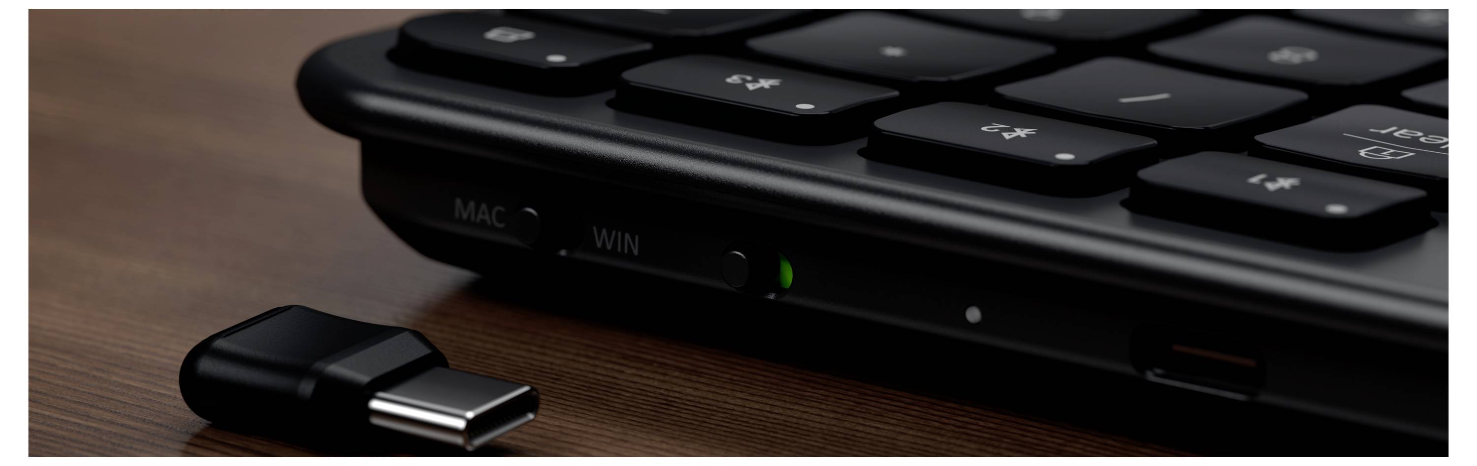 Nahaufnahme der Vorderkante einer Tastatur mit einem angeschlossenen USB-C-Adapter und MAC- sowie WIN-Schaltern auf dem Gerät.