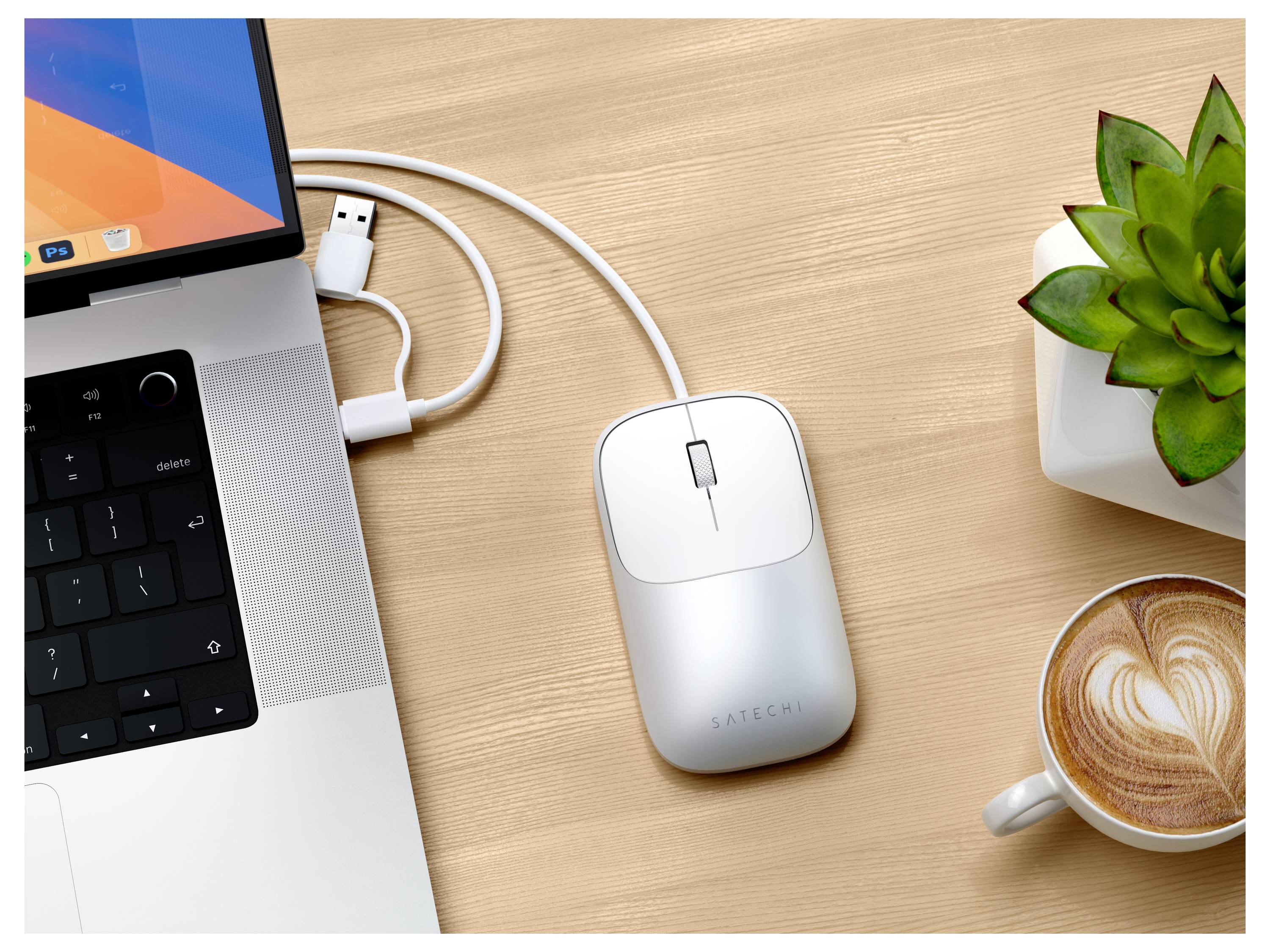 Draufsicht auf einen Laptop, der über ein USB-C-Kabel mit einer kabellosen Maus auf einem Holzschreibtisch verbunden ist, mit einer kleinen Topfpflanze und einer Tasse Latte in der Nähe.