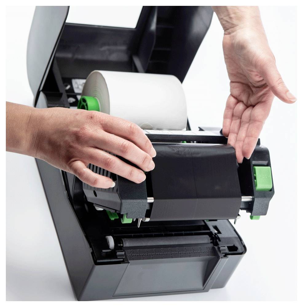 Hände laden eine Etikettenrolle in einen Desktop-Thermodrucker mit einer grünen Kontrolltaste ein.