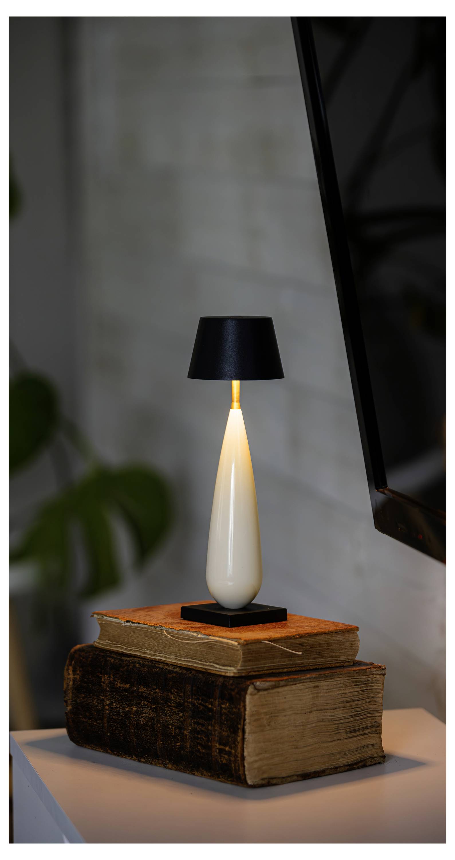Moderne Tischlampe mit schwarzem Schirm leuchtet auf einem Stapel alter Bücher auf einer weißen Oberfläche.