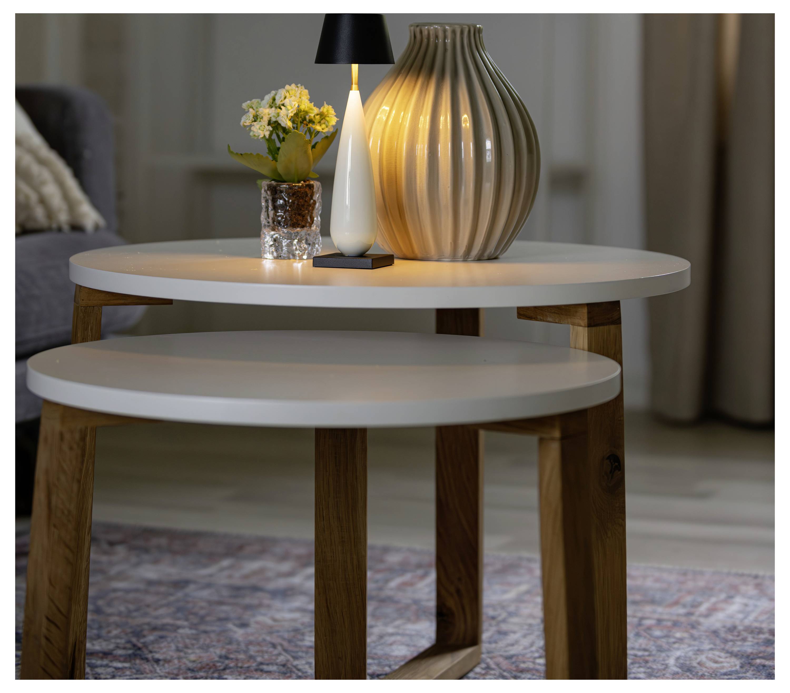 Zwei runde Beistelltische im Wohnzimmer, mit einer Lampe, einer Blumenvase und einer dekorativen Vase auf dem oberen Tisch.