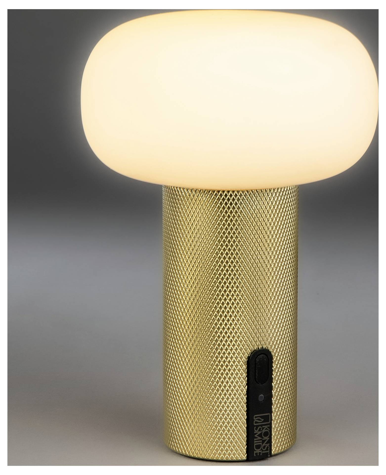 Goldene strukturierte schnurlose Tischleuchte mit leuchtender ovaler weißer Lampenschirm und schwarzem Schalter auf der Basis.