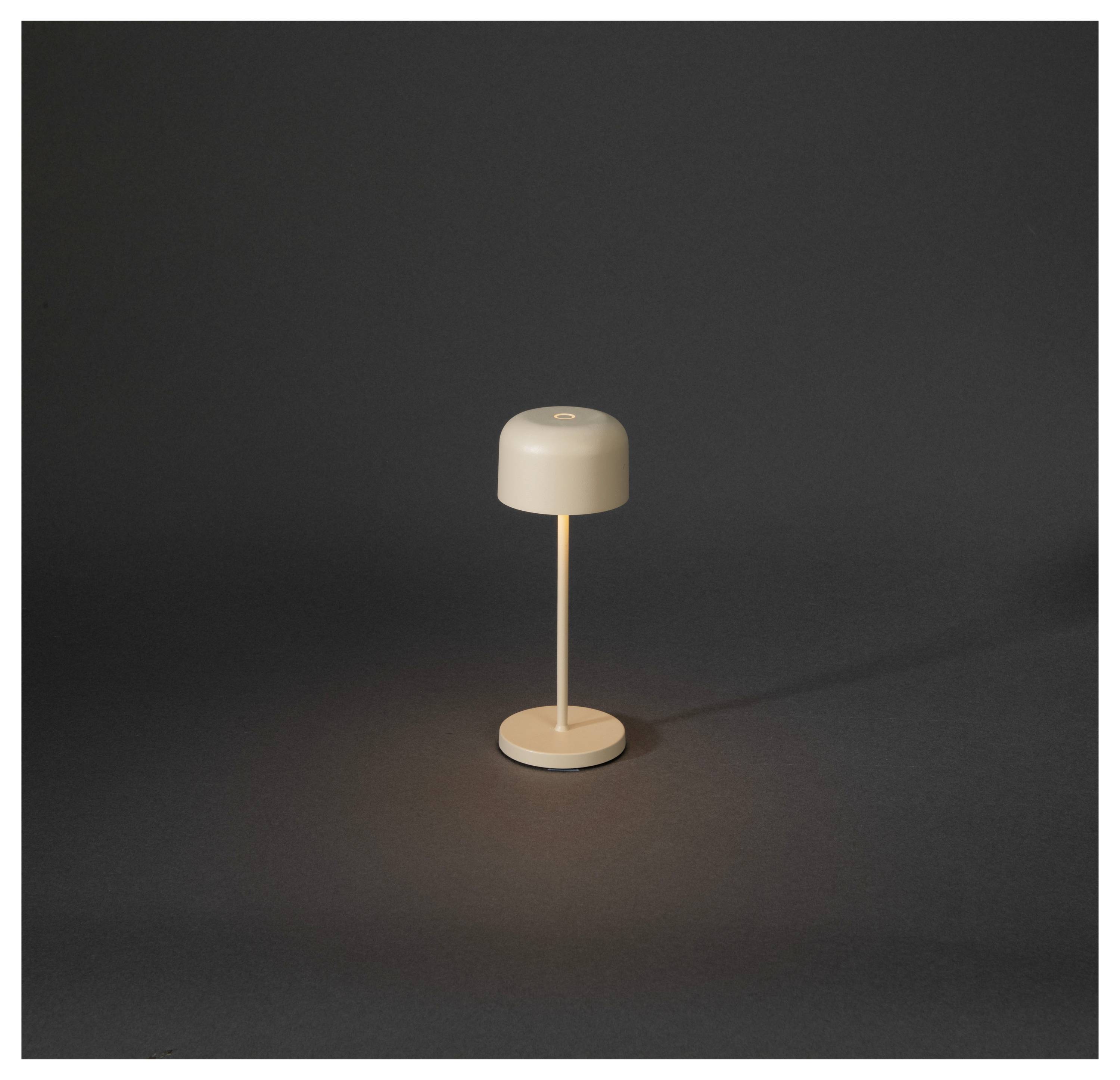 Kleine beige Tischlampe mit zylindrischem Schirm und rundem Sockel, isoliert vor dunklem Hintergrund und sanft beleuchtet.