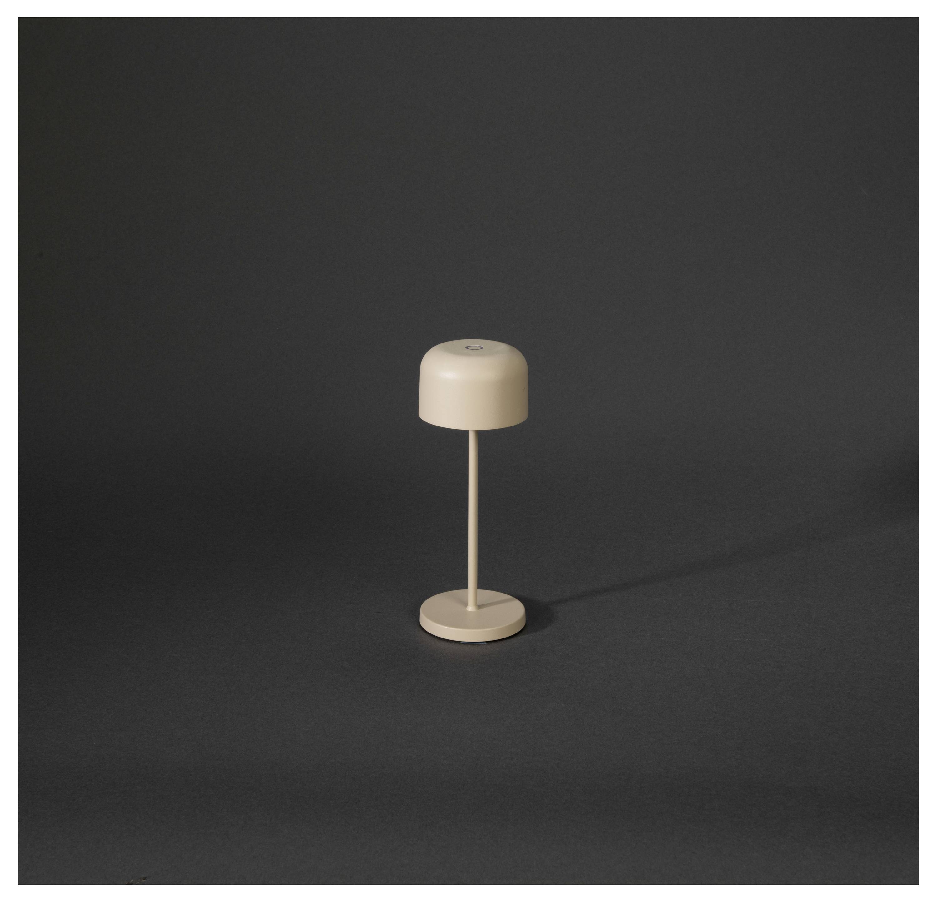 Eine kleine beige schnurlose Tischlampe mit einem abgerundeten Schirm und schlankem Schaft steht zentriert auf einem dunklen Hintergrund.