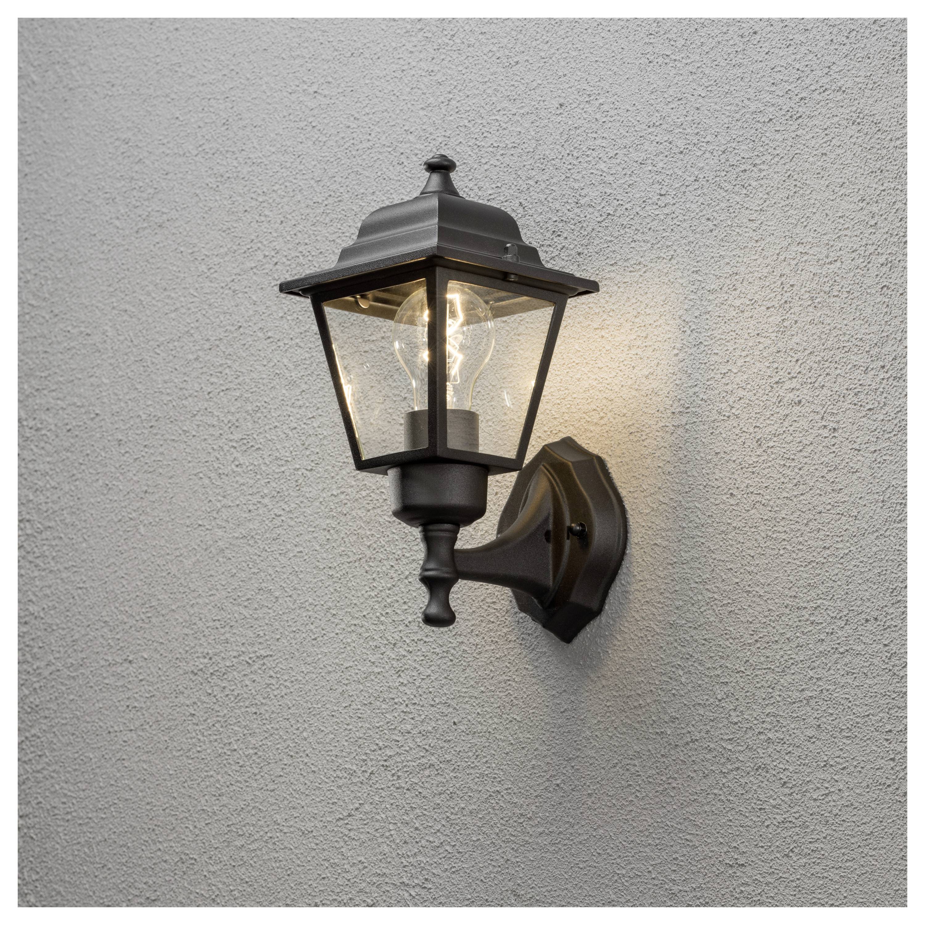 Schwarze beleuchtete Außenwandleuchte an einer hellgrauen Stuckwand, die ein warmes Licht wirft.
