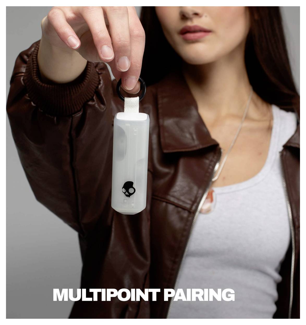 Eine Frau hält ein weißes Bluetooth-Schlüsselanhänger mit dem Text „MULTIPOINT PAIRING" darunter, was auf eine Werbung für eine Kopplungsfunktion hindeutet.