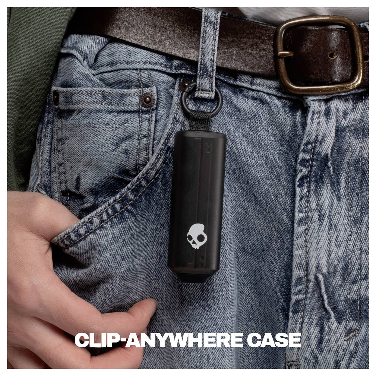 Schwarze Skullcandy-Universalhalterung an einer Gürtels­chlaufe an einer blauen Jeanshose befestigt, mit einer Hand, die die Tasche herauszieht, und dem Text „CLIP-ANYWHERE CASE" unten.