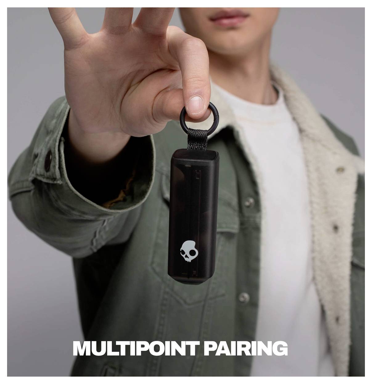 Person, die ein kleines schwarzes Skullcandy-Gerät hochhält, mit dem Text „MULTIPOINT PAIRING" darunter.