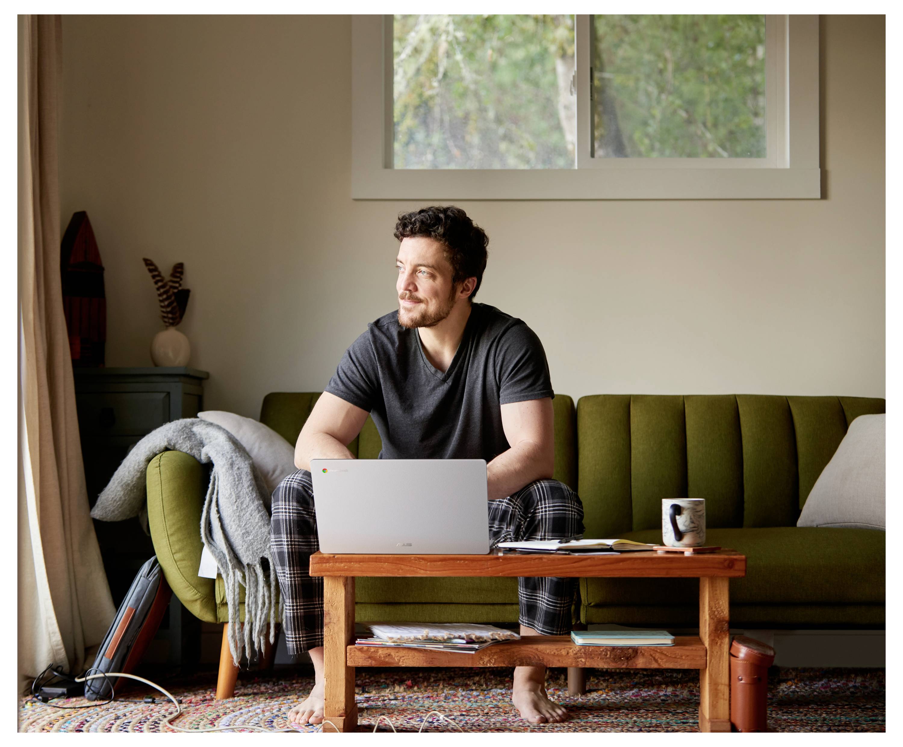 Ein Mann sitzt auf einem Sofa mit einem Laptop und einer Kaffeetasse auf einem Holztisch in einem gemütlichen Wohnzimmer.