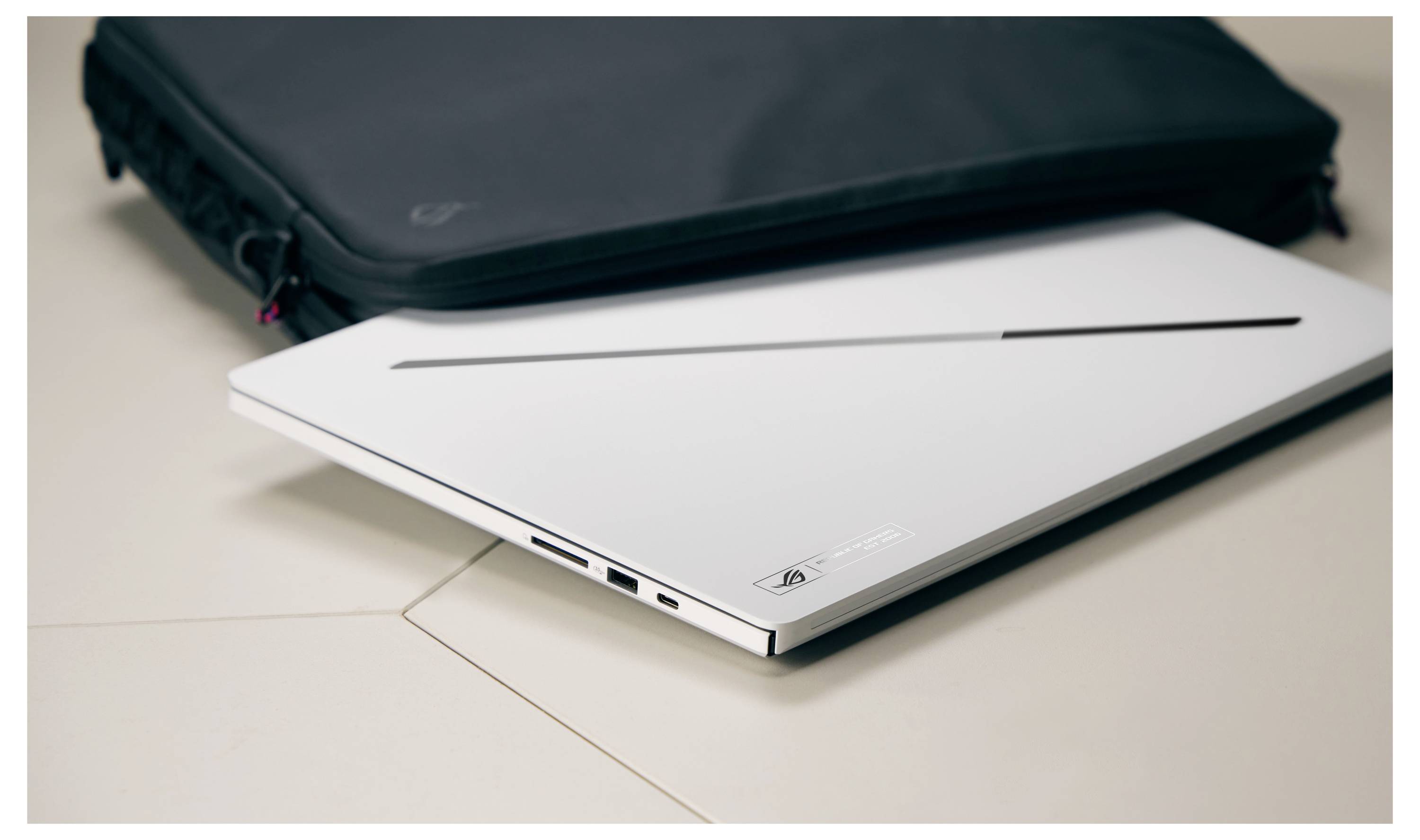 Ein geschlossener weißer Laptop auf einem Schreibtisch mit einer dunklen Transporttasche dahinter.