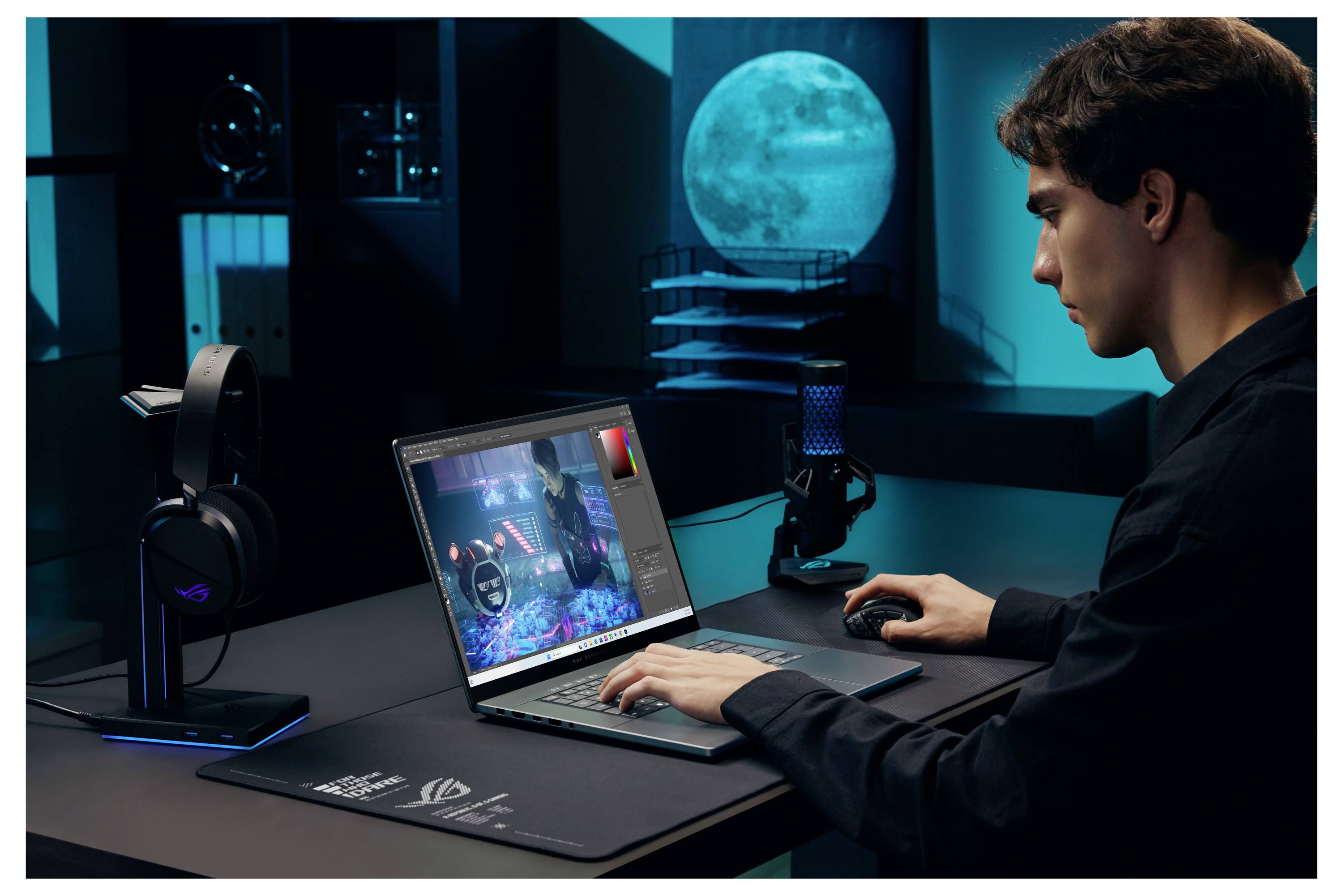 Junger Mann, der in einem dunklen Studio an einem Laptop mit Gaming-ähnlichem Display und Maus sitzt, mit Kopfhörern und Mikrofon in der Nähe und einem mondbeschienenen Fenster im Hintergrund.