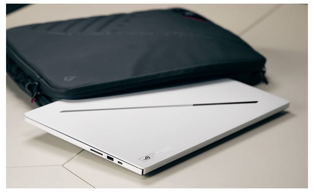 Ein geschlossener weißer Laptop sitzt vor einer schwarzen Transporttasche auf einer gekachelten Oberfläche.