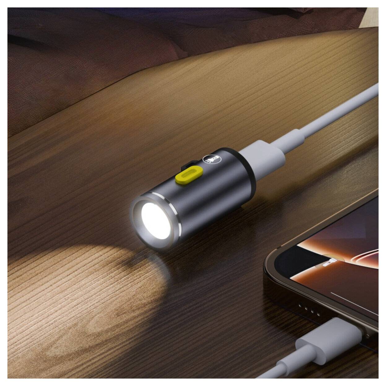 Schwarzer zylindrischer taschenlampenartiger Kabeladapter mit gelbem Knopf, verbunden mit einem Smartphone auf einer Holzoberfläche, leuchtend Licht an der Spitze.