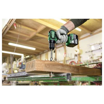 Handschuhbearbeitete Arbeitskraft bohrt einen großen Holzbalken mit einem Akkubohrer in einer Werkstatt.