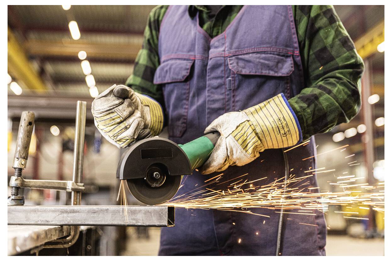 Ein Arbeiter benutzt einen Winkelschleifer auf Metall und sendet Funken über eine Industriewerkstatt.