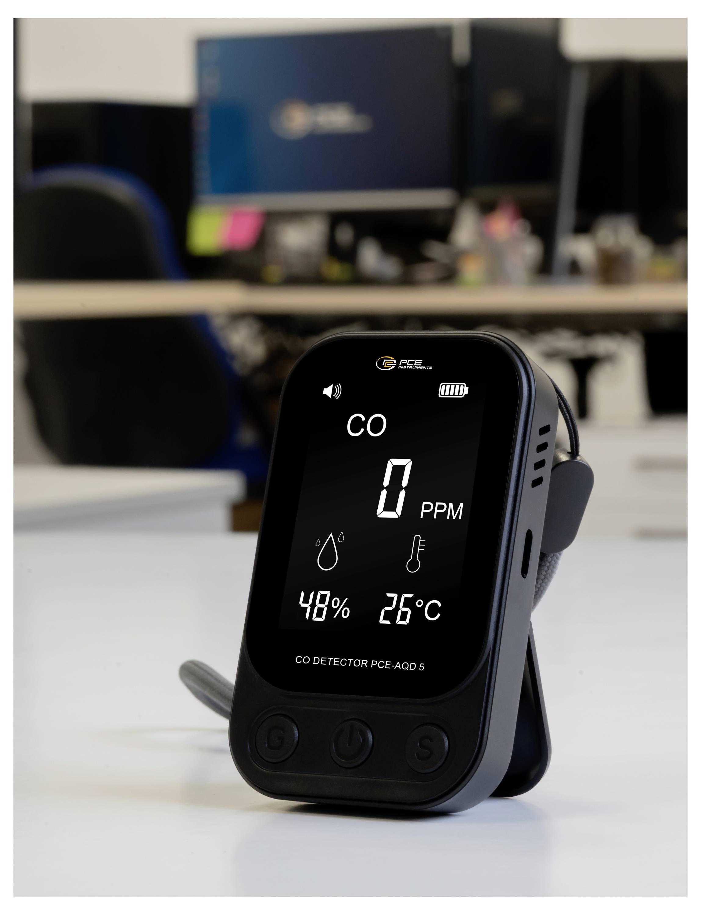 Tragbarer CO-Detektor auf einem Schreibtisch, zeigt auf seinem Display 0 PPM, 48% Luftfeuchtigkeit und 26°C an.