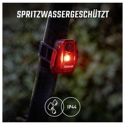 Rote Fahrradlampe am Sattelrohr leuchtet im Regen; Text 'SPRITZWASSERGESCHÜTZT' und Symbol 'IP44' zeigen Spritzwasserschutz.<br>