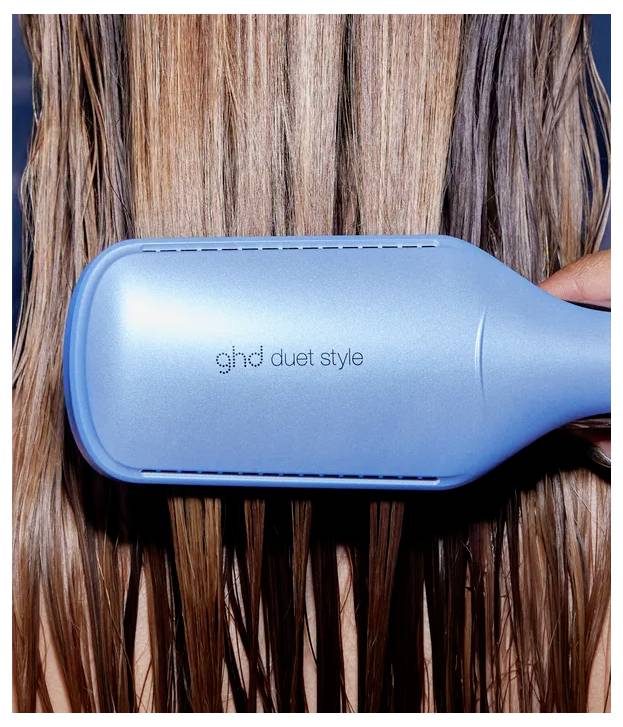 Blauer ghd Duet Style Hair Tool beim Durchbürsten von nassem Haar, gehalten von einer Hand.
