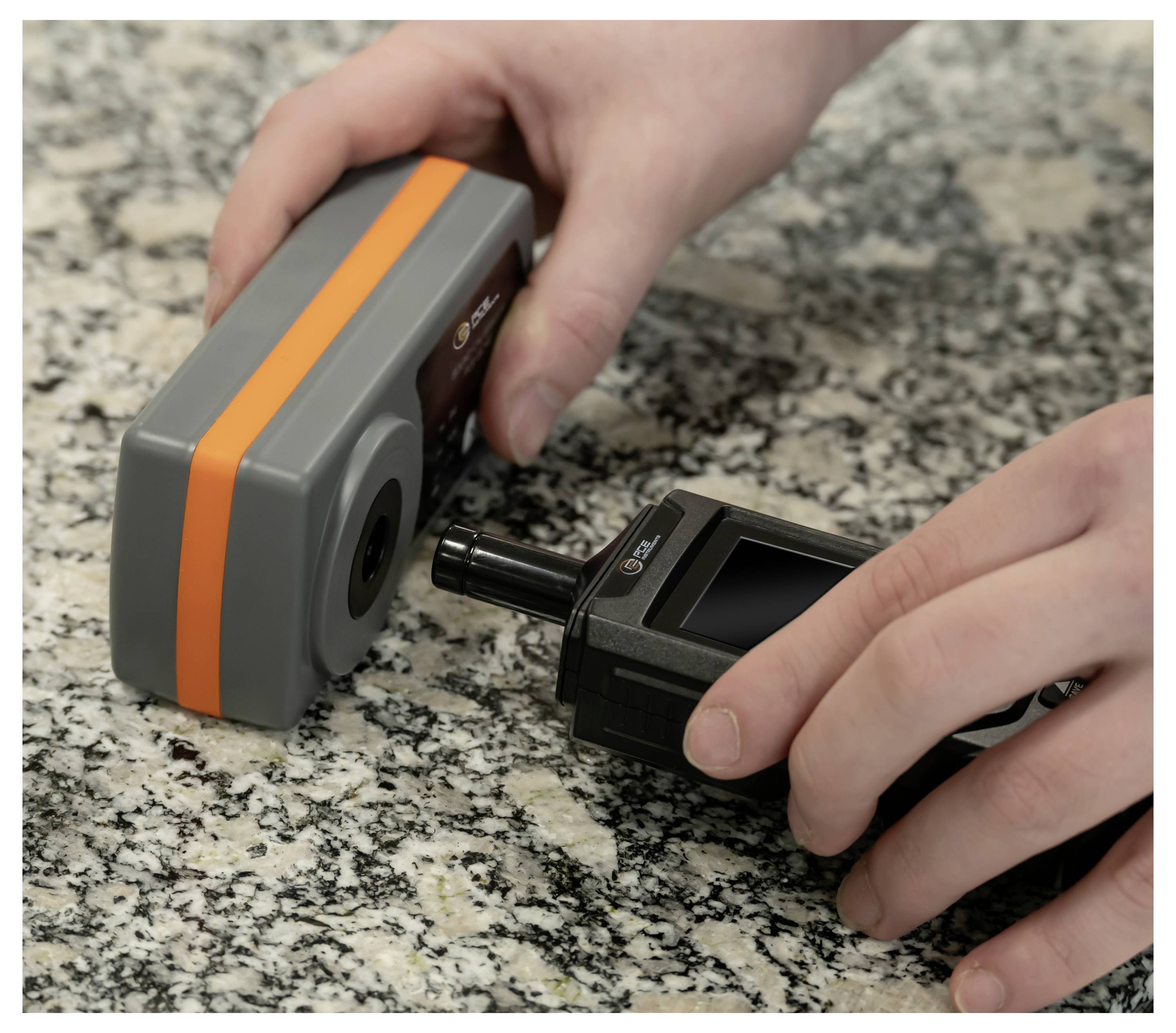 Hände verbinden ein schwarzes tragbares Gerät mit einem grauen Modul mit einem orangefarbenen Streifen auf einer Granitarbeitsfläche.