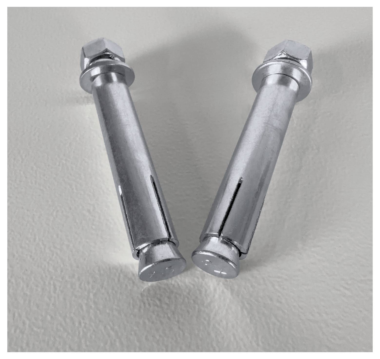 Zwei Metallspreizdübel liegen nebeneinander auf einer hellen Oberfläche.