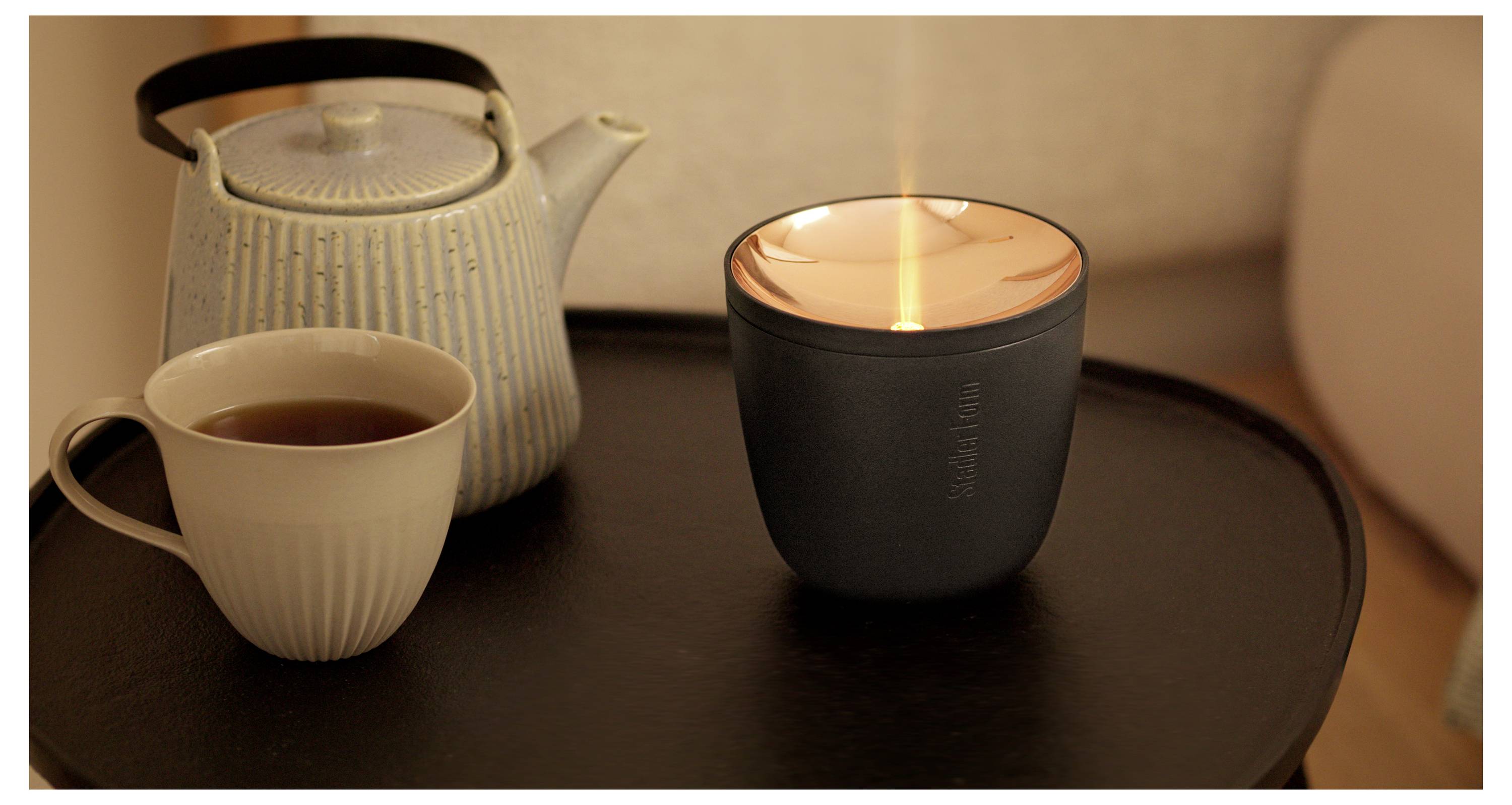 Eine brennende Kerze, eine Teetasse und eine Teekanne auf einem Tablett, die eine gemütliche Teezeit schaffen.