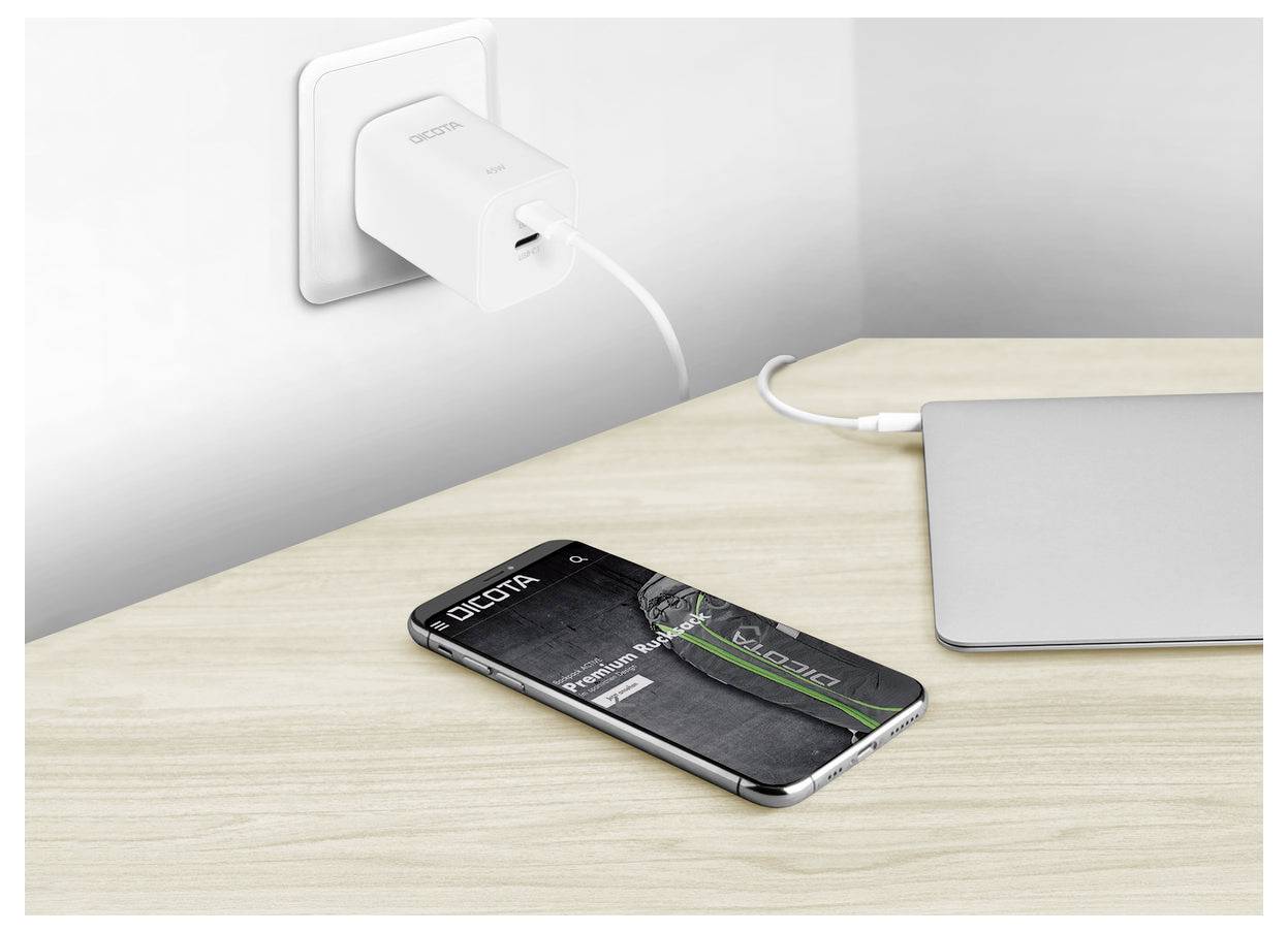 Smartphone lädt auf einem Schreibtisch neben einem Laptop auf, angeschlossen an einen Wandadapter mit einem Kabel; der Bildschirm zeigt eine Batterie-Leistungs-/Schutzhüllengrafik.