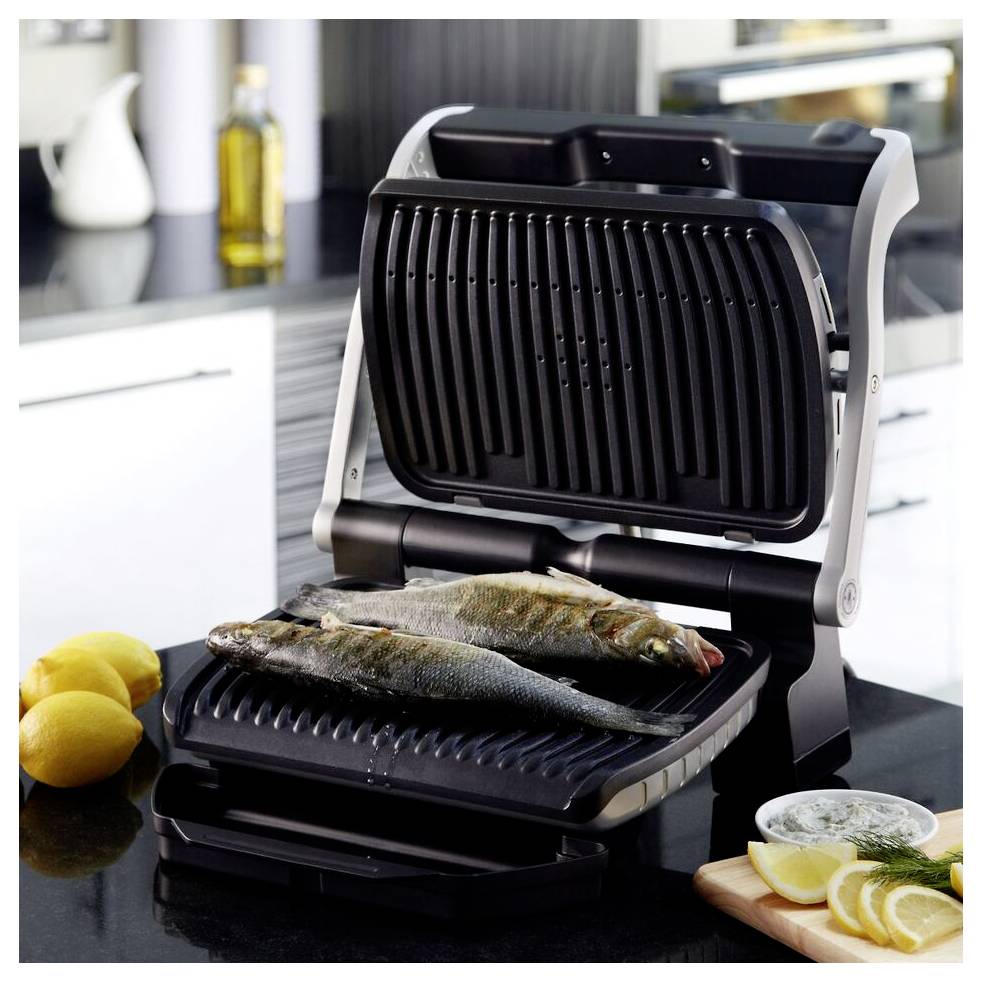 Elektrischer Tischgrill mit zwei ganzen Fischen im Inneren in einer modernen Küche, mit Zitronen und Kräutern in der Nähe.