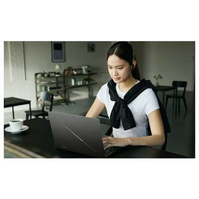 Junge Frau, die an einem Laptoptisch in einem Café arbeitet, mit einer Kaffeetasse neben ihr.