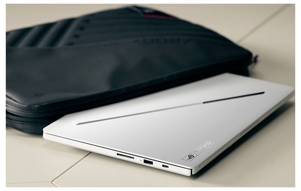 Geschlossener silberner Laptop liegt vor einer schwarzen Tragetasche auf einer hellen Tischplatte.