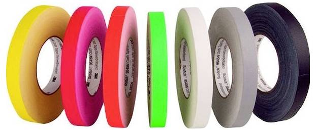 Sieben Rollen farbiges Klebeband in einer Reihe angeordnet, zeigen gelbes, braunes, rosa, rotes, grünes, weißes, graues und schwarzes Klebeband.