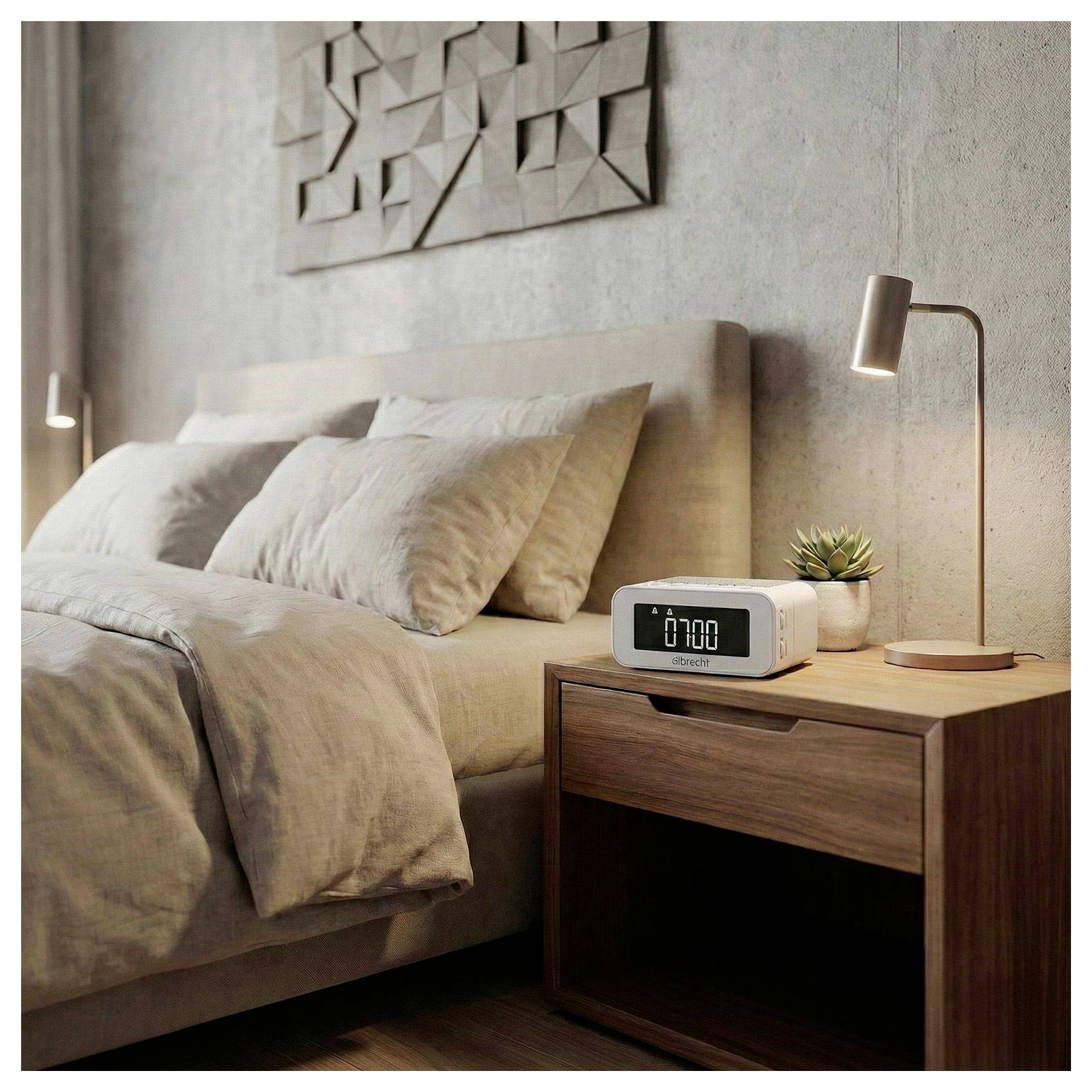 Modernes Schlafzimmer mit unmachtem beigem Bett, holzerner Nachttisch, Digitaluhr, kleiner Pflanze und Nachttischlampe.
