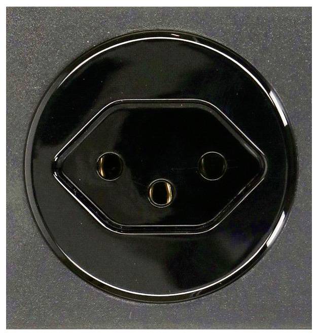 Nahaufnahme einer schwarzen kreisförmigen elektrischen Steckdose mit drei runden Steckerlöchern auf dunklem Hintergrund.