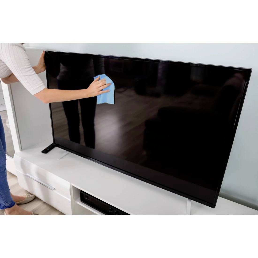 Eine Person, die einen Flachbildfernseher mit einem blauen Tuch auf einem weißen Ständer reinigt.