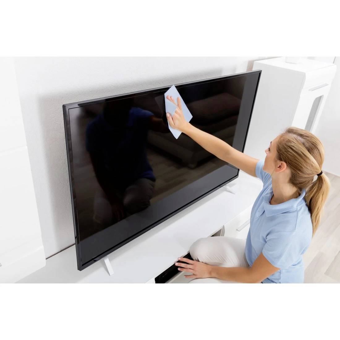 Eine Frau reinigt einen an der Wand angebrachten Flachbildfernseher mit einem Tuch in einem hellen Raum.