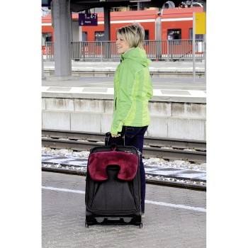 Eine Frau in einer grünen Jacke steht auf einem Bahnsteig und hält einen schwarzen Koffer mit Rollen.