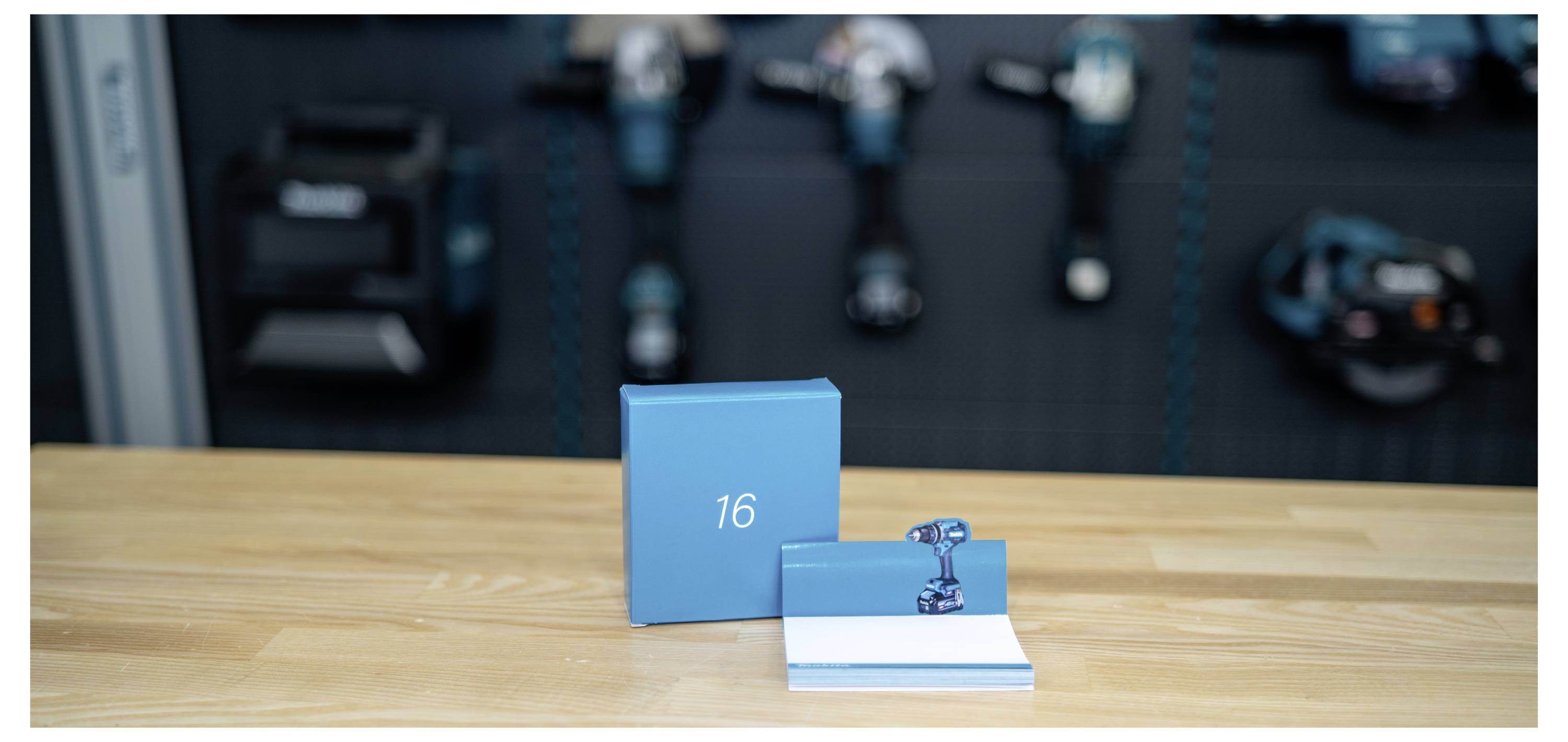 Blaue Produktschachtel und offenes Booklet mit einem kleinen Metallteil, mit der Nummer "16" auf der Schachtel, auf einem Holztisch angezeigt.