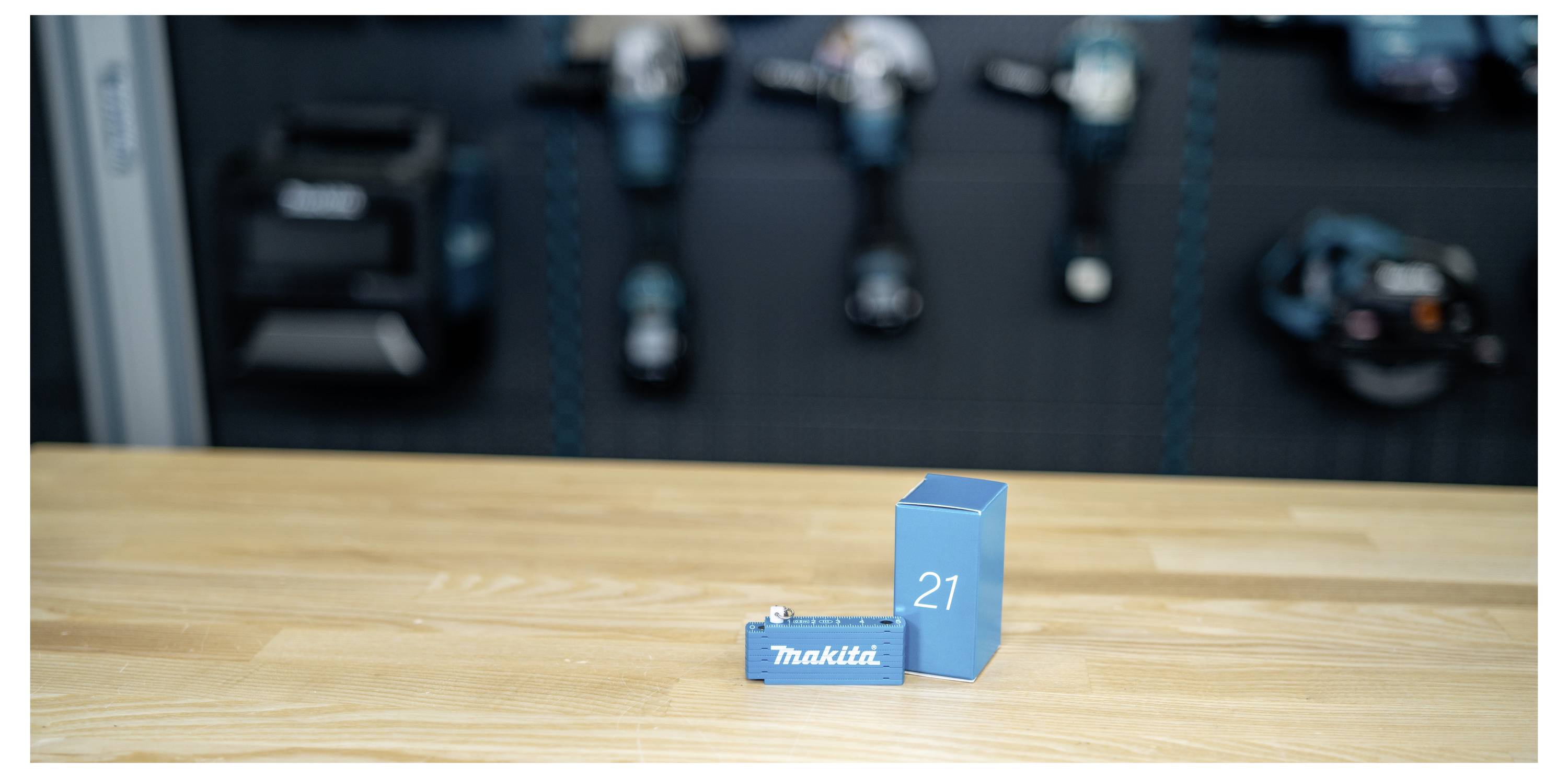 Zwei blaue Makita-Batteriekästen mit den Aufschriften 18V und 21 stehen auf einer Holzwerkbank, mit unscharfen Elektrowerkzeugen im Hintergrund.