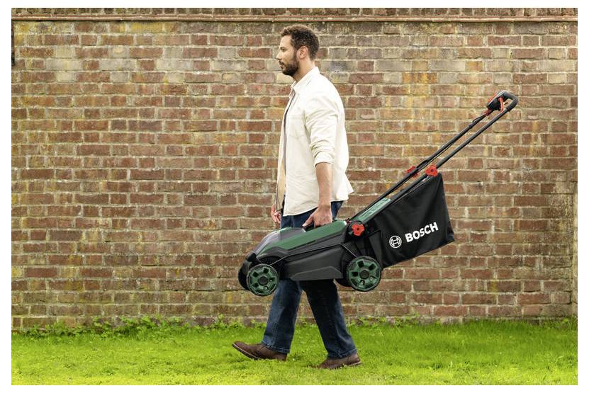 Ein Mann, der neben einer Backsteinmauer geht und einen Bosch-Rasenmäher auf Gras trägt, was tragbare Gartengeräte veranschaulicht.