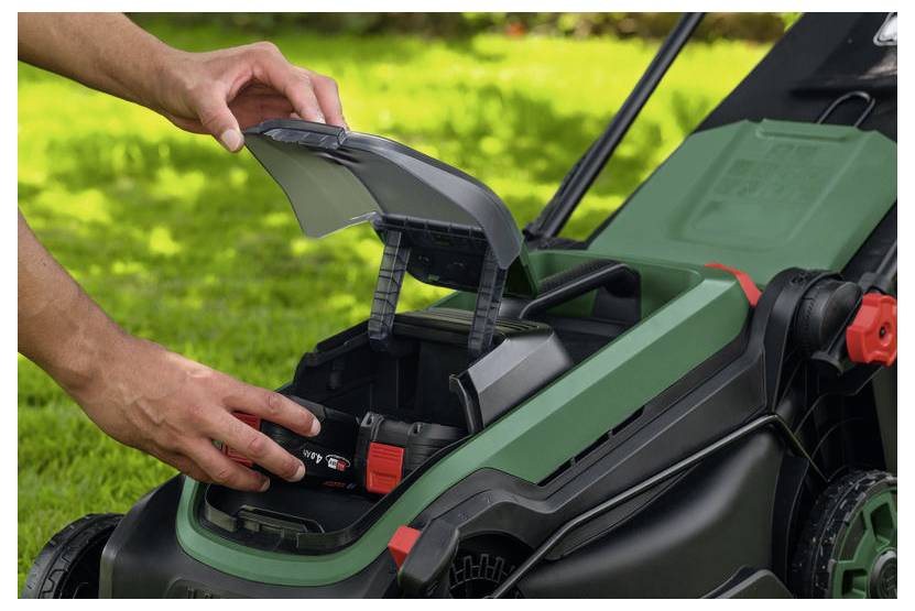 Hände legen eine Batterie in ein offenes Fach eines schnurlosen Rasenmähers im Freien ein.
