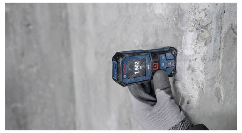 Hand mit Handschuh, die einen digitalen Wandscanner verwendet, um verborgene Ständer oder Leitungen in einer Betonwand zu lokalisieren.
