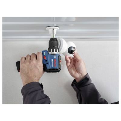 Hände verwenden einen Bosch-Akkubohrer, um eine an der Decke montierte Halterung für eine Sicherheitskamera zu installieren.