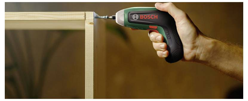 Eine Hand, die einen kabellosen Bosch-Akkubohrer hält und damit eine Schraube in einen hölzernen Schrankrahmen während der Möbelmontage treibt.