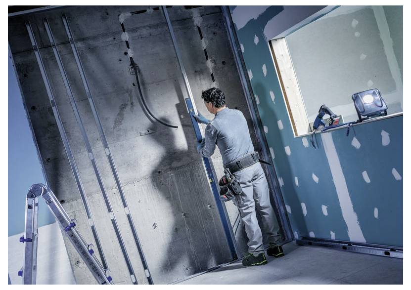 Arbeiter installiert Wandrahmung in einem unvollendeten Raum und verwendet dabei eine Wasserwaage neben einer Betonwand und Gipskartonplatten.