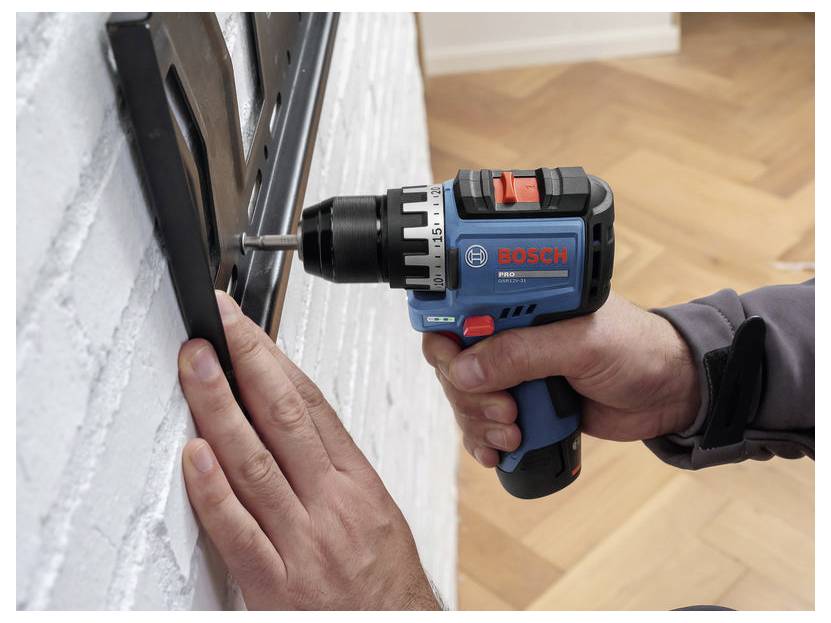 Eine Person bohrt mit einem Bosch Akkubohrer eine Schraube in eine weiße Wand, während sie das schwarze Panel an Ort und Stelle hält.