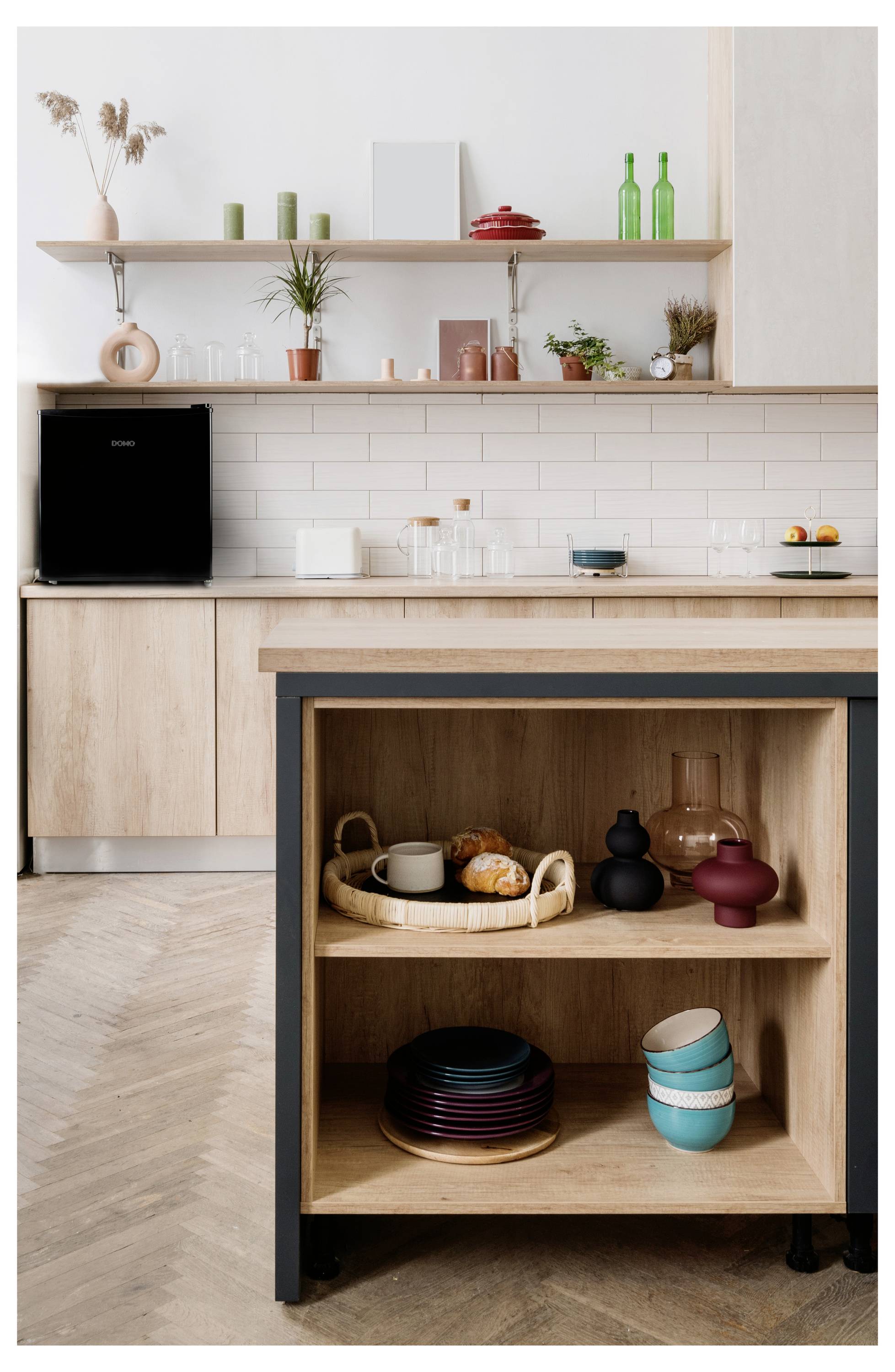 Moderne Küche mit hellem Holzschrank, offenen Regalen, schwarzem Gerät und einer zentralen Insel mit stapelgeschirr und Servierschüsseln.