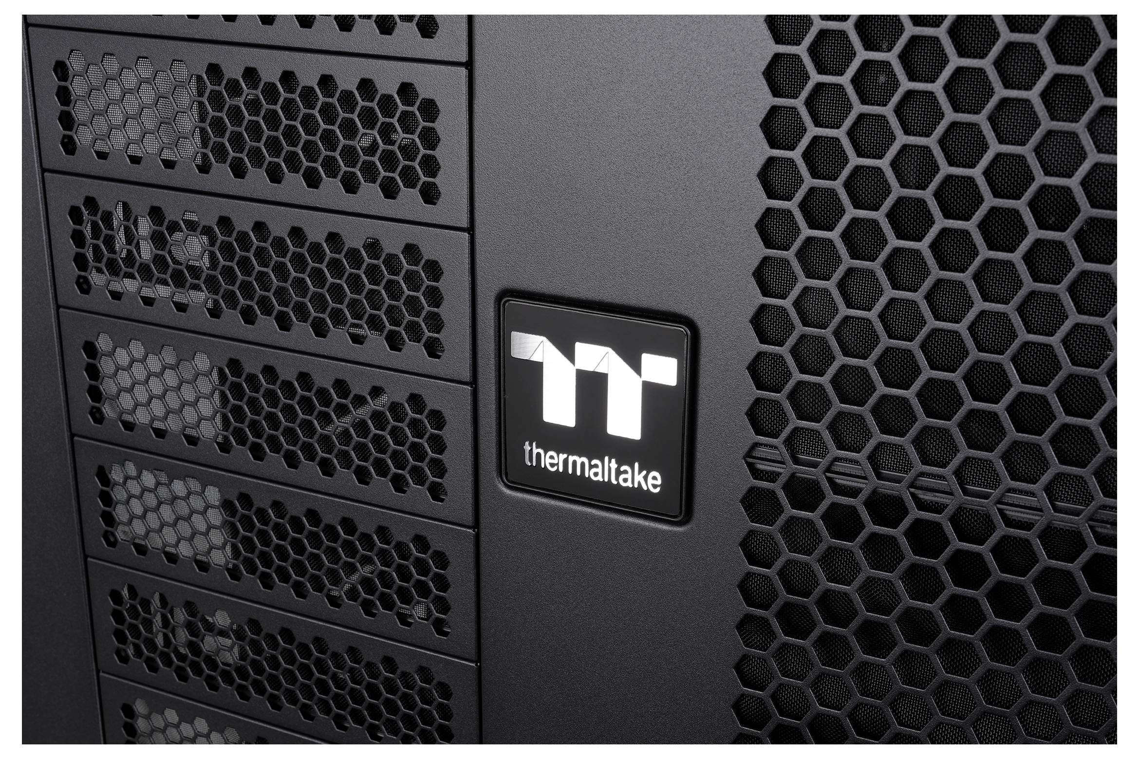 Nahaufnahme eines Thermaltake-Computergehäuse-Frontpanels mit hexagonalen Mesh-Lüftungsgittern und Laufwerk-Schachtabdeckungen.