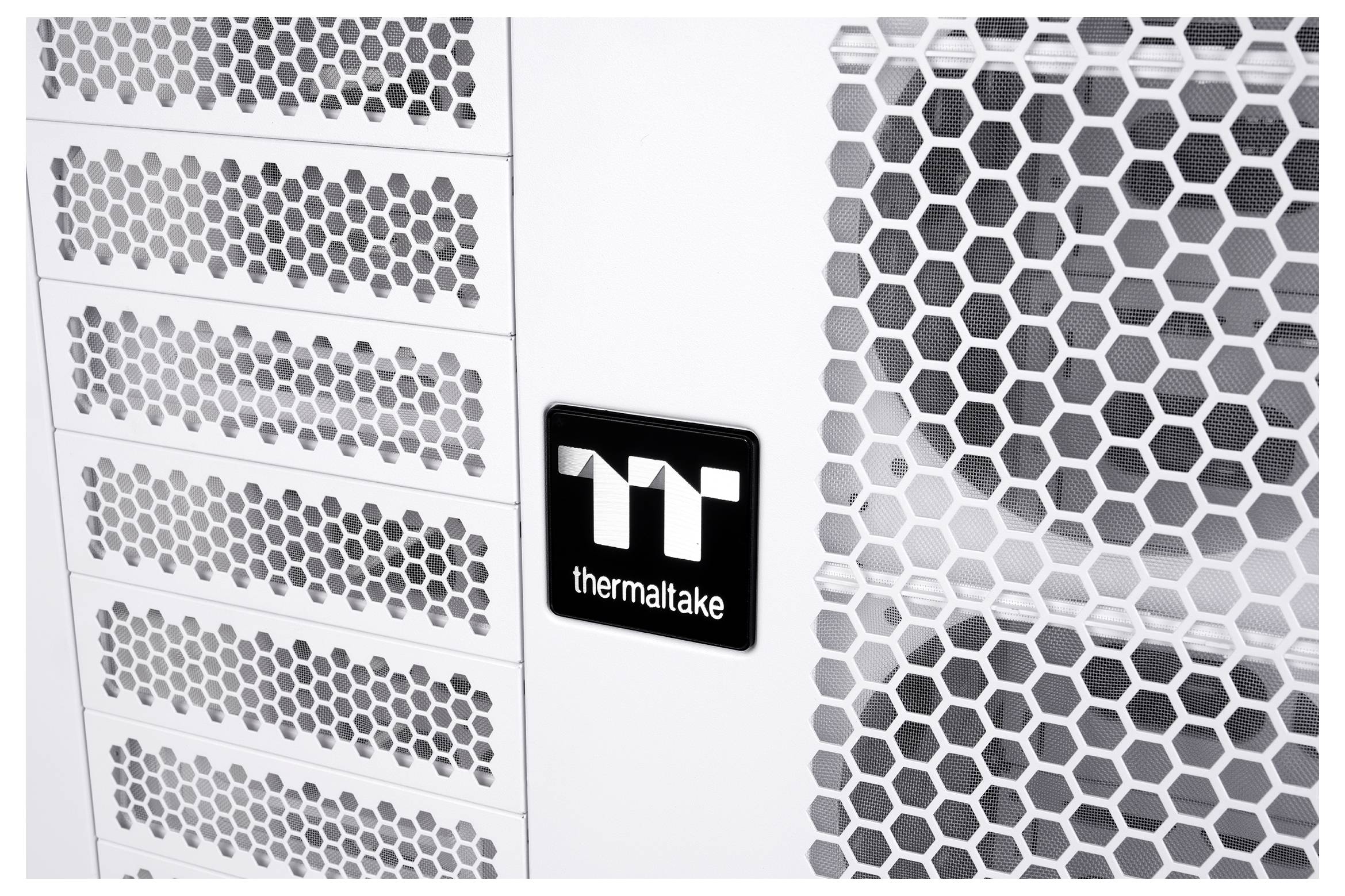 Nahaufnahme eines Thermaltake-PC-Gehäuses mit weißen sechseckigen Mesh-Lüftungspanelen und einem zentralen "Thermaltake"-Logo-Abzeichen.