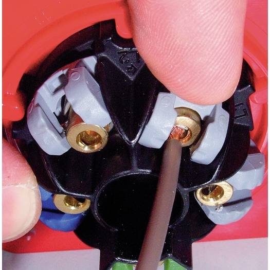Nahaufnahme einer Person, die einen Draht in einen schwarz-roten Elektrosteckerverbinder mit Messingschraubenklemmen einfügt.